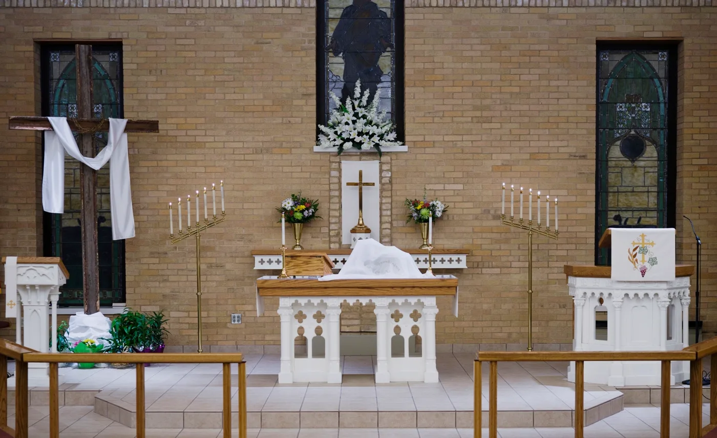 A church altar prepared with candles, flowers, and a cross