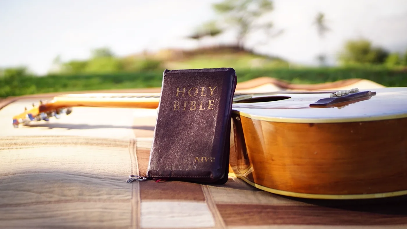 A Bible resting beside an acoustic guitar in warm natural light
