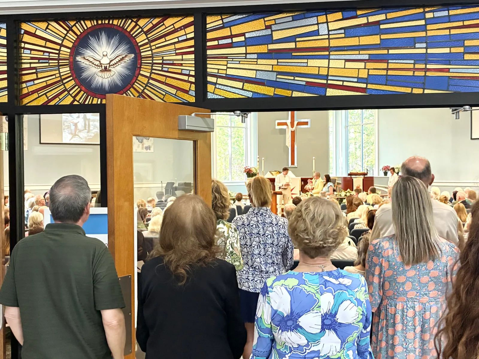 Congregation entering the sanctuary at Christ Church Bluffton beneath a stained glass window of a dove