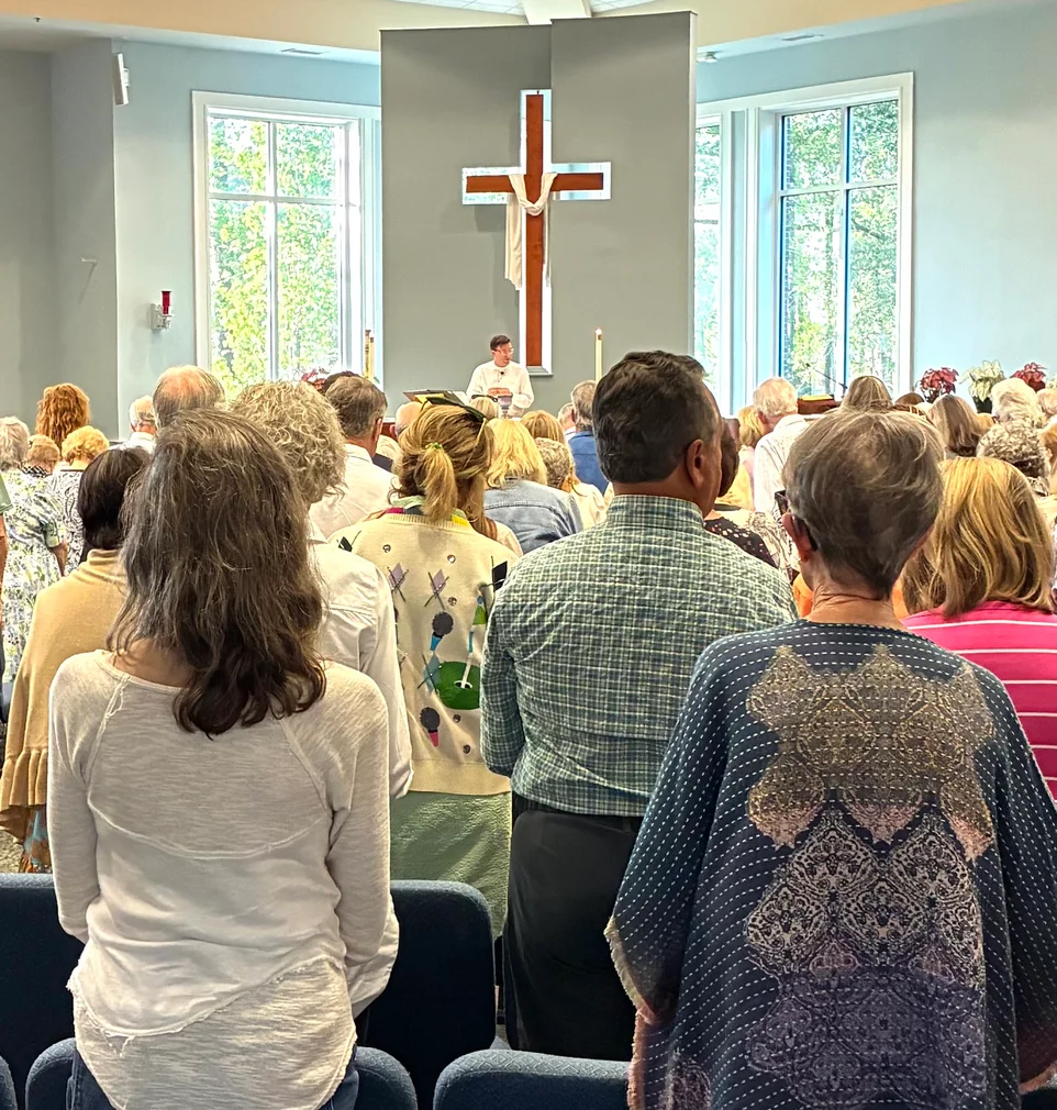 Pastor Jonathan preaching before the cross at Christ Church Bluffton, congregation standing in worship